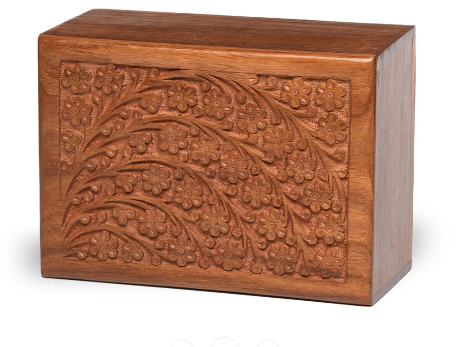 A rectangular wooden keepsake box with a lid, featuring an intricate hand-carved floral and leaf pattern on the front panel, shown against a plain white background.